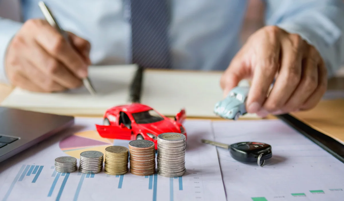 Man calculating car costs with model cars and stacked coins on a financial document."